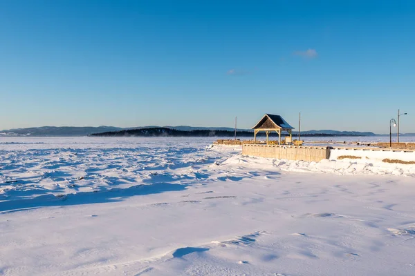 Kışın günbatımında, Bas-Saint-Laurent 'te, kar ve buzun ortasında, arka planda (le aux Corneilles) Charlevoix ve (le aux Corneilles) karga adası ile Kamouraska limanının iskelesi (Quebec, Kanada)..