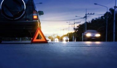 Kırmızı acil durum dur işareti (kırmızı üçgen uyarı işareti) ve kır yolunda kırık siyah SUV arabası.