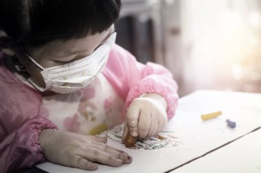Portrait of lovely  Asian girl wearing facial hygienic mask  and drawing her art work with crayons ,selective focus. Quarantine