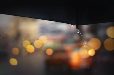 Mavi şemsiyeli yağmurlu bir gece. Şehir hayatı yumuşak odaklı ve çok sığ bir alan derinliğinde..