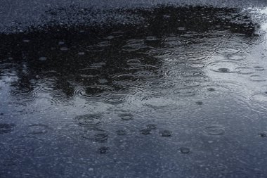 Yağmur damlaları ve yansıma asfalt yoldaki büyük bir su birikintisinde, yağmurlu mevsim arka planında.