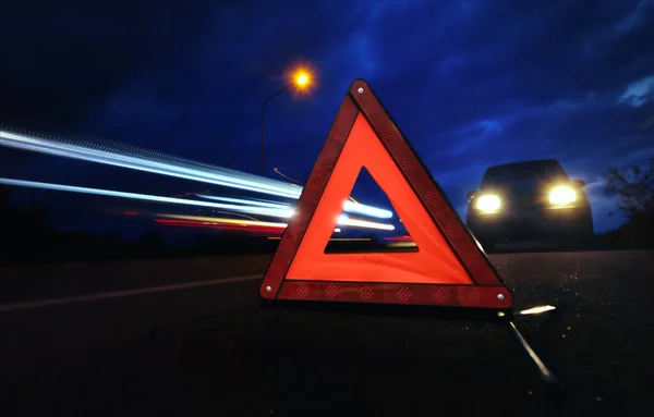Kırmızı acil durum dur işareti (kırmızı üçgen uyarı işareti) ve gece geç saatlerde trafik ışığı izlerinin uzun pozlandırılması.