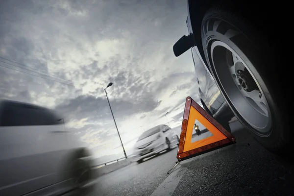 Kırmızı acil durum dur işareti (kırmızı üçgen uyarı işareti) ve güzel gün batımı gökyüzü, seçici odak ve uzun deklanşör hızı ile köprü üzerinde kırık siyah SUV araba.