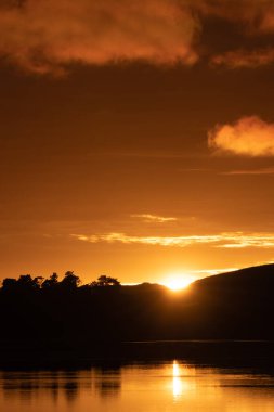 Altın güneş körfezin üzerinden yükseliyor alçak tepelerin siluetinden su boyunca, dikey bileşim.