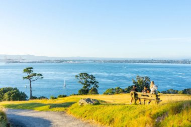 Mount maunganui New Zealand - January 2 2022; Three people sitting on bench beside track up Mount Maunganui looking out to view up Tauranga Harbour.