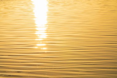 Ripples on surface of golden water with rising sun glow brightly shining through.