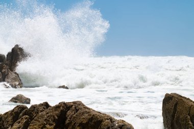 Büyük dalgalar kayalık kıyı şeridine çarpıyor ve Yeni Zelanda 'daki Maunganui Dağı' na püskürtüyor..