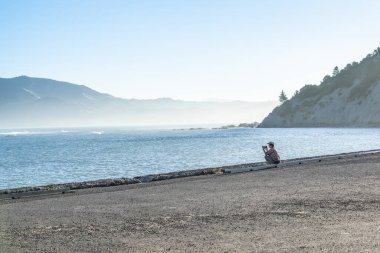 Tokomaru Körfezi 'nde güneş batarken ve uzak tepelerin altındaki deniz sislerini aydınlatırken.