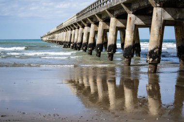Uzun yapısal desen, ıslak kumda yansıma ve azalan perspektif ve Tolaga Körfezi İskelesi 'nin altındaki yapının gölgesi, Doğu Kıyısı Yeni Zelanda.