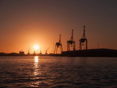 Konteynır vincleri, gün batımının derinliklerinde gökyüzü ve ışık ile Tauranga Limanı 'ndaki Sülfür Noktasında dururlar..