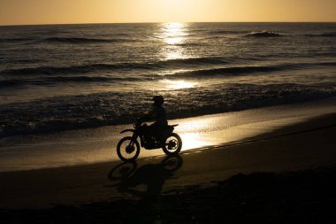 Whanganui Yeni Zelanda - 9 Nisan 2022; Şafak vakti Castlecliff plajı üzerinde hız yapan siluetli motosikletli