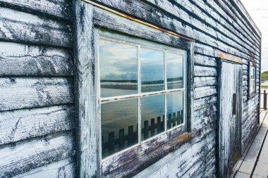 Eski kereste iskelesinin penceresinde yansıyan gölcükler Yeni Zelanda 'nın batısındaki küçük Okarito kasabasındaki lagünün üzerine dökülüyor..
