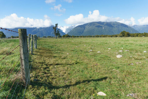 Fence line posts and wire disappear into distance along field with Southern Alps and Fox Glacier South Island New Zealand.