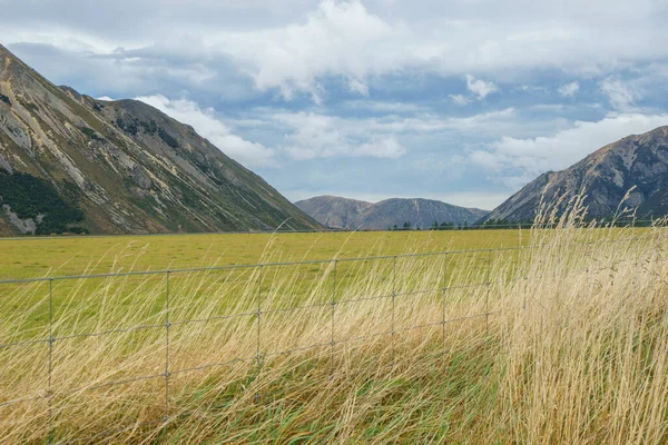 Expansive green flat grassland between mountain ranges under overcast sky at Craigieburn, Canterbury New Zealand
