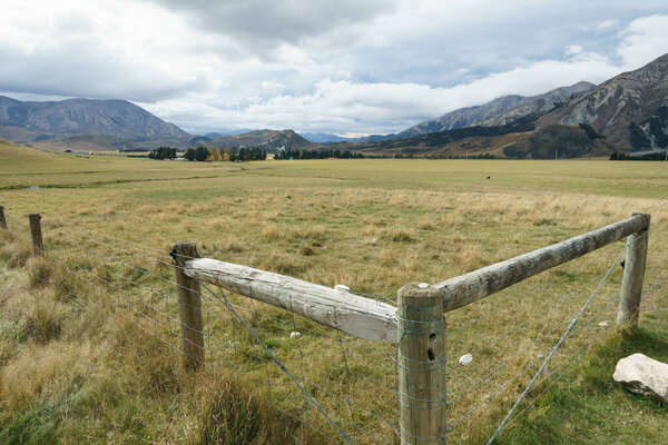 Corner fence strainers and farmland leading to mountains under cloudy sky and expansive farm girls through distant mountains under cloudy sky, Castle Hill Canterbury New Zealand.