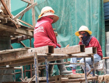 Bangkok Tayland - 10 Ağustos 2007; İnşaat alanında demir kirişlerin üzerinde oturan şapka ve yüz maskesi takan iki kadın