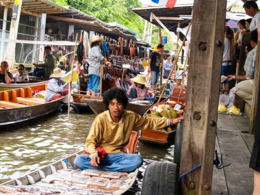 Bangkok Thailand - 10 Ağustos 2007; Adam kayığının üzerinde Süzülen Pazarlar 'da önplanda hareketli bir geçmişe sahip ürünlerle oturuyor
