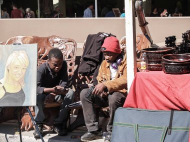 Johannesburg Güney Afrika - 12 Ağustos 2027; Yerel sanat ve zanaatla el sanatları pazarının tezgahında oturan iki genç bir tabanca tarafından tutulan tabancaya bakıyor.