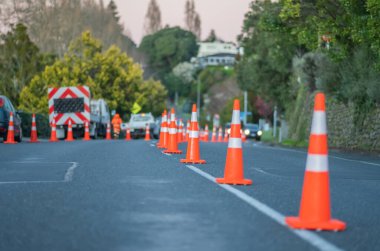 Bright orange road cones reduce street lanes while workers trim edge