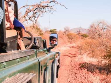 Madikwe South Africa - August 15 2007; Traveling along red soil bush track on safari with tourist reflected in mirror.