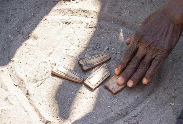 Black African hand playing game in circle in dust on ground moving wooden piece in Botswana village.