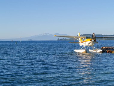 Taupo New Zealand - January 11 2002; Tourist float plane at pier refueling on on popular traveler attraction with mountains in distance across lake.
