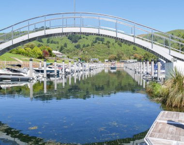 Arching pedestrian bridge structure over marina with moored and arriving boats