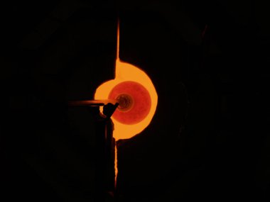 Taupo New Zealand - January 13 2008; Glassblower with dark protective eye glasses and with molten glass shape on long pole turning and shaping it