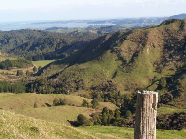 Fore ground rustic post and Rural farmland and view down valley to coast on west coast North Island near Raglan.