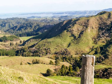 Foreground focus on rustic post and Rural farmland and view down valley to coast on west coast North Island near Raglan.