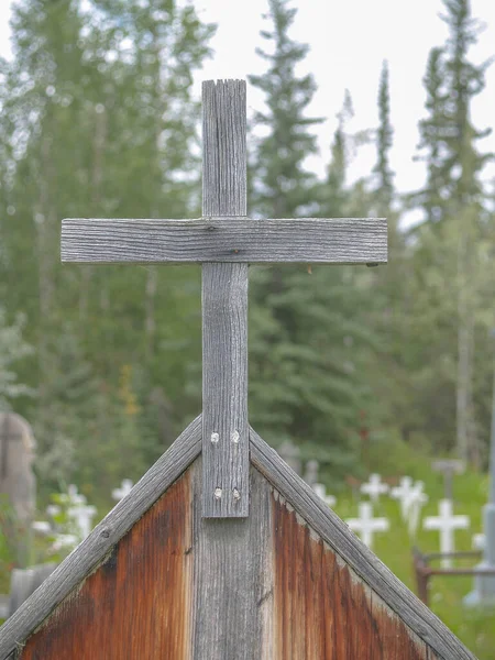 Old wooden. cross close up with defocused field of white crosses of graveyard.in Dawson City.