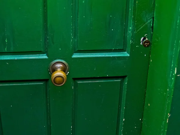 Closeup of paneled closed green door with round brass knob