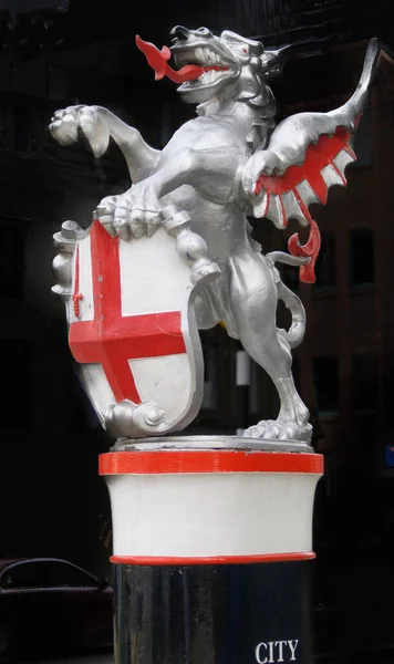 Dragon. and red cross shield of London City on plinth in city. with large red tongue out, United Kingdom.