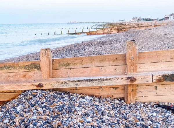 日の出に石のビーチを越えて海につながるワーキングビーチ木製の防波堤 イギリス — ストック写真