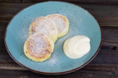 Siyah tahtaya ekşi krema sürülmüş süzme peynirli krep ve siyah arkaplan, üzerine pudra şekeri serpiştirilmiş.