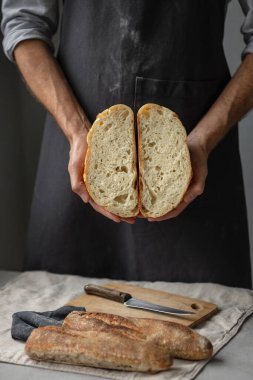 Yetişkin bir Avrupalı erkek fırıncı elinde yuvarlak taze bir ekmek tutuyor. Fırında bir adam mayalı ekmek ve baget tutuyor.. 