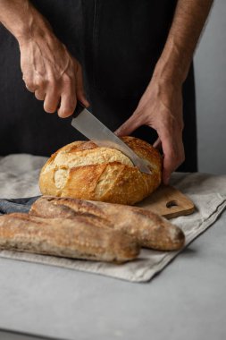 Yetişkin bir Avrupalı erkek fırıncı elinde yuvarlak taze bir ekmek tutuyor. Fırında bir adam mayalı ekmek ve baget tutuyor.. 