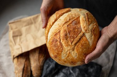 Yetişkin bir Avrupalı erkek fırıncı elinde yuvarlak taze bir ekmek tutuyor. Fırında bir adam mayalı ekmek ve baget tutuyor.. 