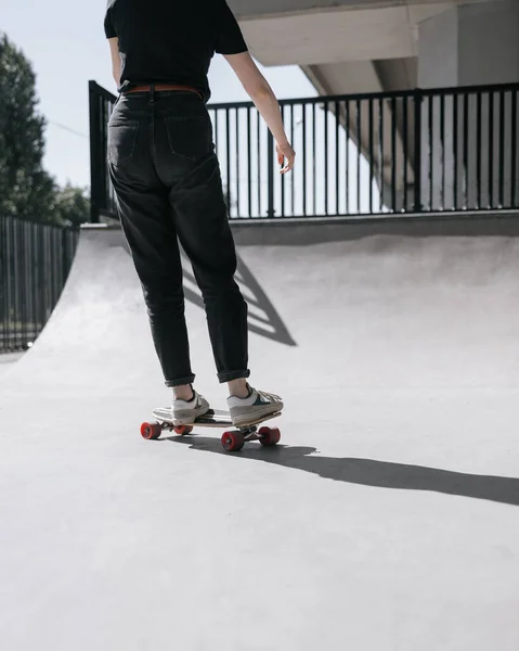 En europeisk kvinnlig skridskoåkare med rött hår åker skateboard på en skridskobana. en kvinna i svarta kläder och en skateboard eller en longboard bedriver aktiv idrott — Stockfoto