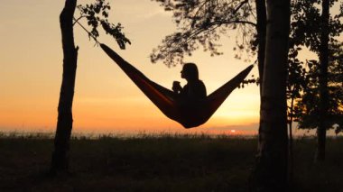 Avrupalı bir kadın doğada bir hamakta gitar çalıyor ve şarkı söylüyor. bir kadın seyahat blogcusu video içeriği oluşturur