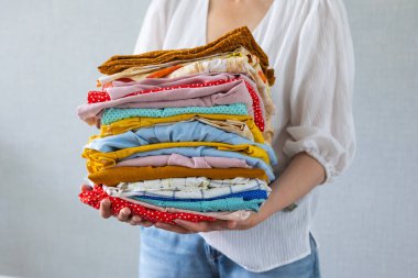 Avrupalı bir kadın çamaşırhanede yıkanmak ya da geri dönüşüm için elinde bir sürü renkli kıyafet tutar.