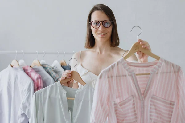 Uma mulher europeia estilista profissional com cabelo escuro e óculos escolhe roupas para uma reunião de negócios ou jantar. — Fotografia de Stock