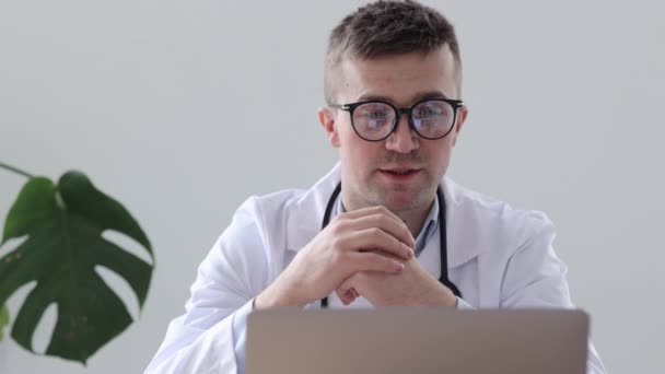 Médico europeo en una clínica hablando con un paciente a través de un enlace de vídeo, un médico caucásico en un consultorio en un hospital diagnostica a un paciente a través de una webcam — Vídeos de Stock