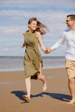 Bir çift adam ve bir kadın sahilde yürüyorlar ya da deniz kıyısı boyunca kum boyunca koşuyorlar. güzel ve genç 