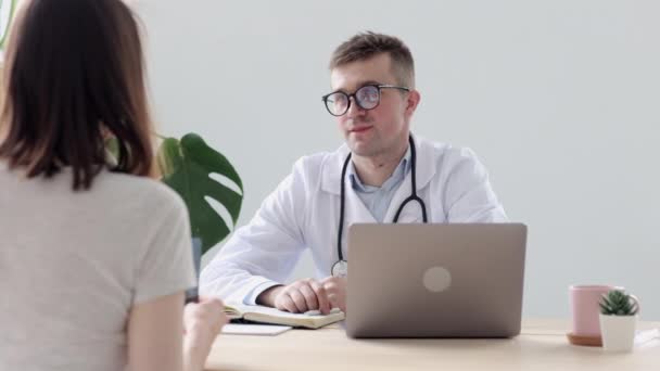 Doctor in a white coat and glasses talking to his patient in a hospital office or clinic — Stock Video
