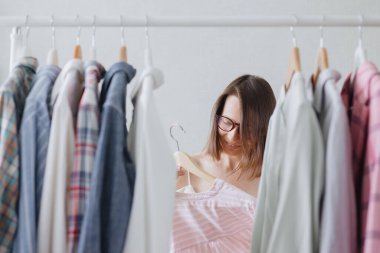 Siyah saçlı ve gözlüklü Avrupalı bir kadın profesyonel stilist iş toplantısı veya akşam yemeği için kıyafet seçer. 
