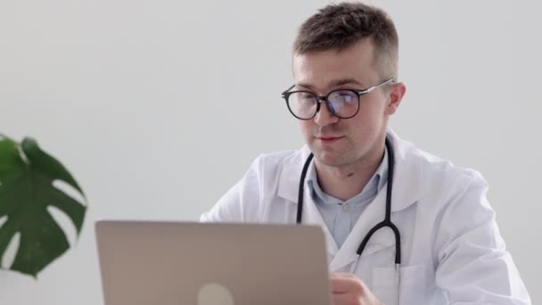 Европейский врач в клинике разговаривает с пациентом по видеосвязи, кавказский врач в офисе в больнице диагностирует пациента через веб-камеру — стоковое видео
