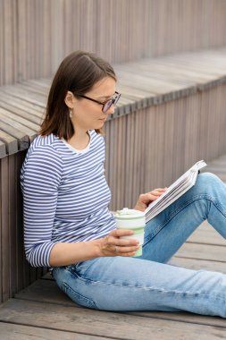 Genç ve kendinden emin bir Avrupalı kadın dinleniyor ve kitap okuyor. Bir kadın kahve içer, rahatlar ya da arkadaşlarıyla buluşmayı bekler.