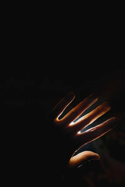 the hand covers the bright light of the spotlight. a beautiful combination of light and shadow. the hand of a man or woman on a bright light background