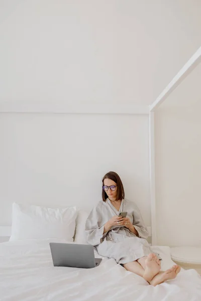 회색 아마포 옷을 입은 유럽 여성 이 집에서 노트북 컴퓨터를 다루거나 휴식을 취하고 있다. 천 년 대여성 이 노트북으로 영화를 보면서 재미를 보고 있습니다. — 스톡 사진